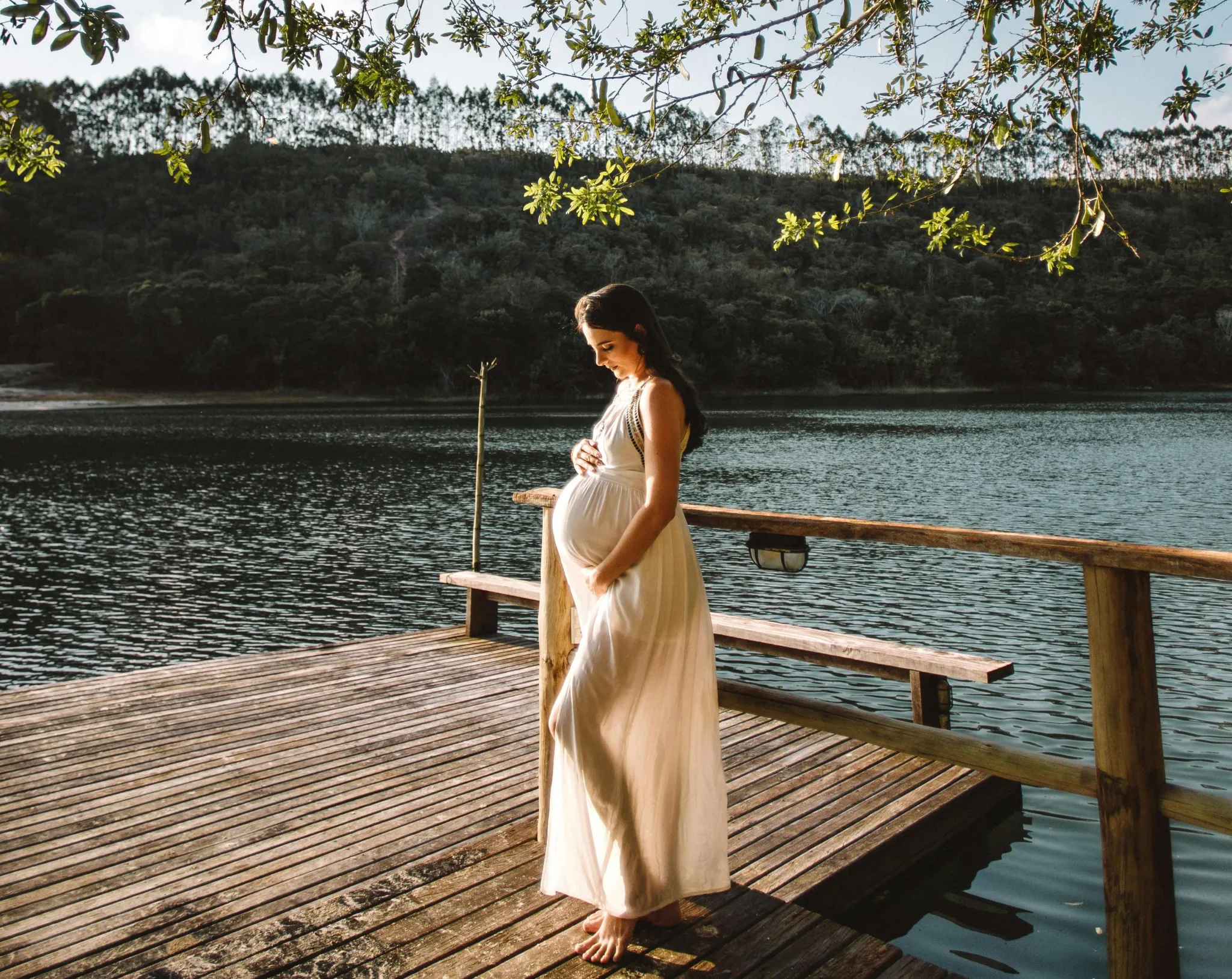 Femme enceinte en robe blanche sur un ponton au bord d'un lac